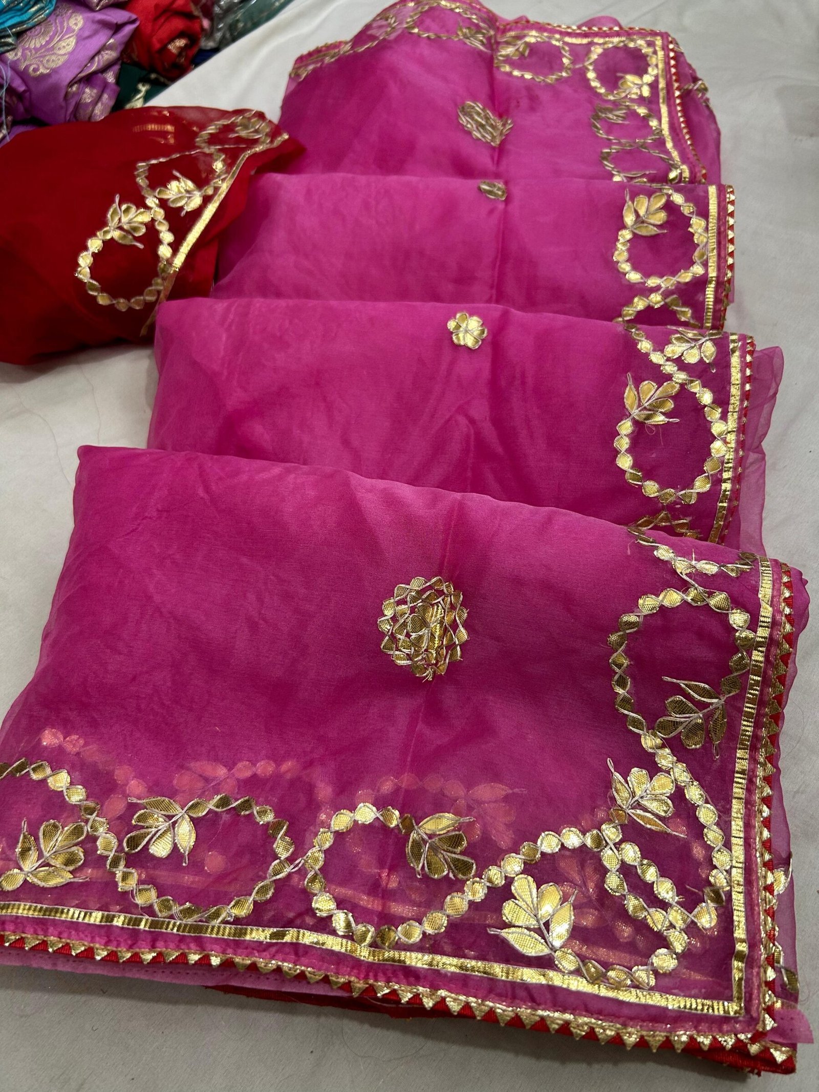 Elegant Organza Gota Patti Handwork Saree 7 A vibrant orange organza saree with intricate silver Gota Patti handwork laid out next to a deep red blouse piece.