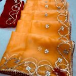 A beautiful deep purple Organza saree with detailed gold Gota patti handwork and a contrasting bright blue blouse piece.