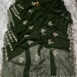 A deep green Royal Georgette saree with all-over handwork floral motifs and a detailed cutwork border laid on a marble surface.
