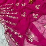 A deep green Royal Georgette saree with all-over handwork floral motifs and a detailed cutwork border laid on a marble surface.