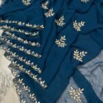 A deep green Royal Georgette saree with all-over handwork floral motifs and a detailed cutwork border laid on a marble surface.