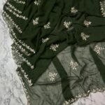 A deep green Royal Georgette saree with all-over handwork floral motifs and a detailed cutwork border laid on a marble surface.