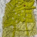A deep green Royal Georgette saree with all-over handwork floral motifs and a detailed cutwork border laid on a marble surface.