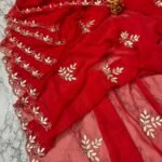 A deep green Royal Georgette saree with all-over handwork floral motifs and a detailed cutwork border laid on a marble surface.
