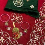 A beautiful red Karwachauth special saree with intricate green and gold Kachhi Gota Patti work, paired with matching bangles and a Kamar satka.