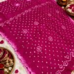 A beautiful bright blue Jodhpuri Bandhani saree made of Nazneen chiffon displayed with traditional decor, flowers, and bangles.