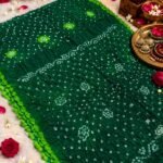 A beautiful bright blue Jodhpuri Bandhani saree made of Nazneen chiffon displayed with traditional decor, flowers, and bangles.