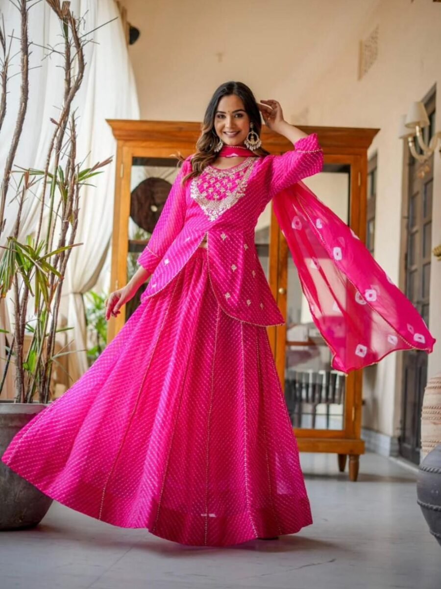A woman wearing a vibrant pink Leheriya printed lehenga set with heavy embroidery and a matching bandhej dupatta.