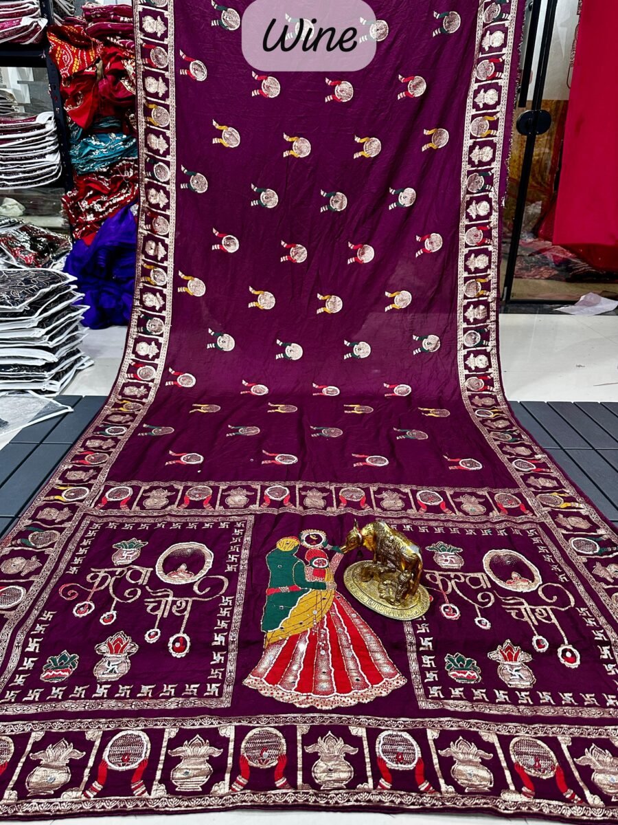 A wine coloured Dola silk saree featuring mirror work, zari butti, and an embroidered border laid out flat.