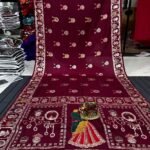 A wine coloured Dola silk saree featuring mirror work, zari butti, and an embroidered border laid out flat.