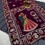 A wine coloured Dola silk saree featuring mirror work, zari butti, and an embroidered border laid out flat.