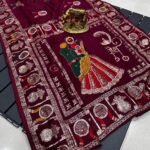 A wine coloured Dola silk saree featuring mirror work, zari butti, and an embroidered border laid out flat.