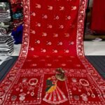A wine coloured Dola silk saree featuring mirror work, zari butti, and an embroidered border laid out flat.
