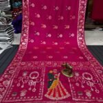 A wine coloured Dola silk saree featuring mirror work, zari butti, and an embroidered border laid out flat.