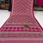 A wine coloured Dola silk saree featuring mirror work, zari butti, and an embroidered border laid out flat.