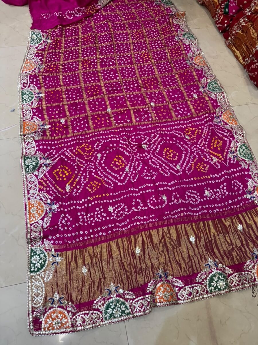 A beautiful deep pink Modal Gaji silk saree with intricate Bandhani patterns, Ghatchola checks, and heavy Zardozi peacock border work.