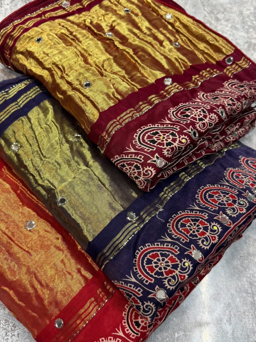 New Arrivals 43 A close-up of a beautifully folded Modal Gajji Silk saree featuring rich golden and red hues with traditional mirror work and intricate hand-print patterns.