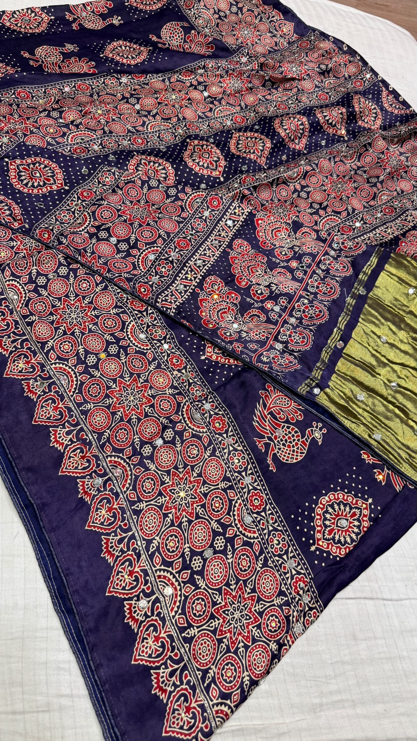 Pure Modal Gajji Silk Mirror Work Saree 2 A close-up of a beautifully folded Modal Gajji Silk saree featuring rich golden and red hues with traditional mirror work and intricate hand-print patterns.