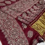 A close-up of a beautifully folded Modal Gajji Silk saree featuring rich golden and red hues with traditional mirror work and intricate hand-print patterns.