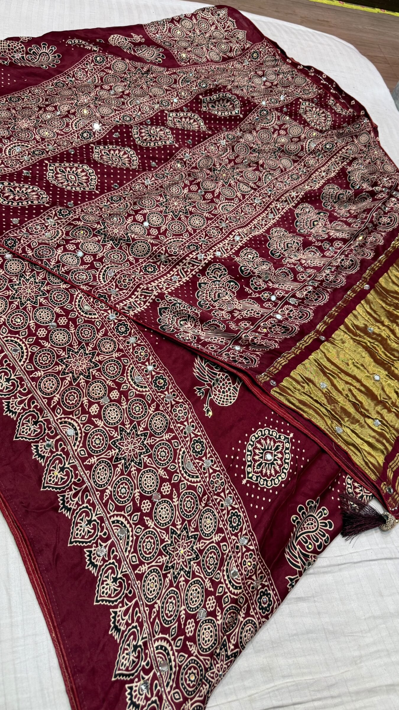 Pure Modal Gajji Silk Mirror Work Saree 4 A close-up of a beautifully folded Modal Gajji Silk saree featuring rich golden and red hues with traditional mirror work and intricate hand-print patterns.