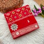A vibrant red Patola print saree with gota patti work folded on a white faux fur rug next to a basket and purple tulips.