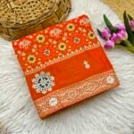 A vibrant red Patola print saree with gota patti work folded on a white faux fur rug next to a basket and purple tulips.