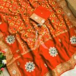 A vibrant red Patola print saree with gota patti work folded on a white faux fur rug next to a basket and purple tulips.
