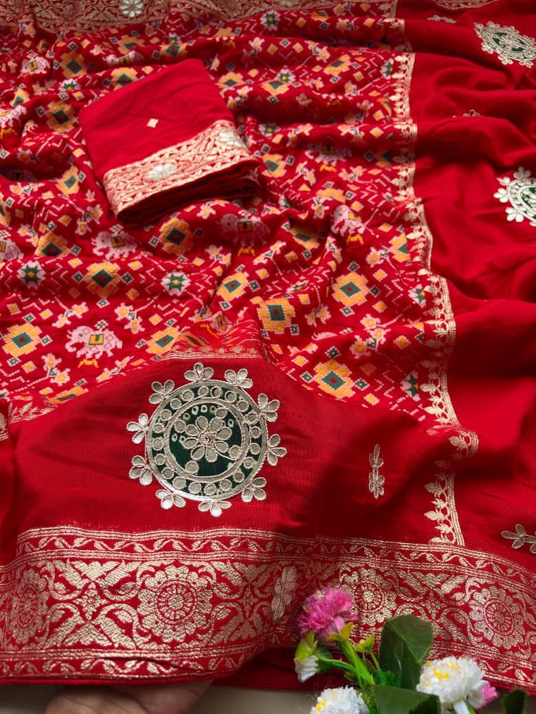 Patola Saree with Gota Patti Work on Viscose Dolla Silk 4 A vibrant red Patola print saree with gota patti work folded on a white faux fur rug next to a basket and purple tulips.