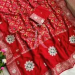 A vibrant red Patola print saree with gota patti work folded on a white faux fur rug next to a basket and purple tulips.
