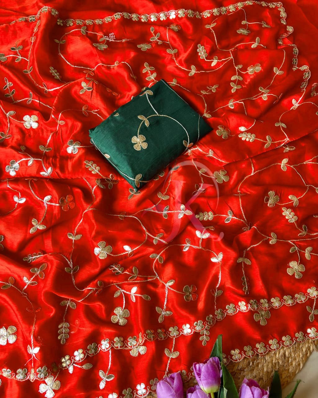Patola Saree with Gota Patti Work on Viscose Dolla Silk 6 A vibrant red Patola print saree with gota patti work folded on a white faux fur rug next to a basket and purple tulips.