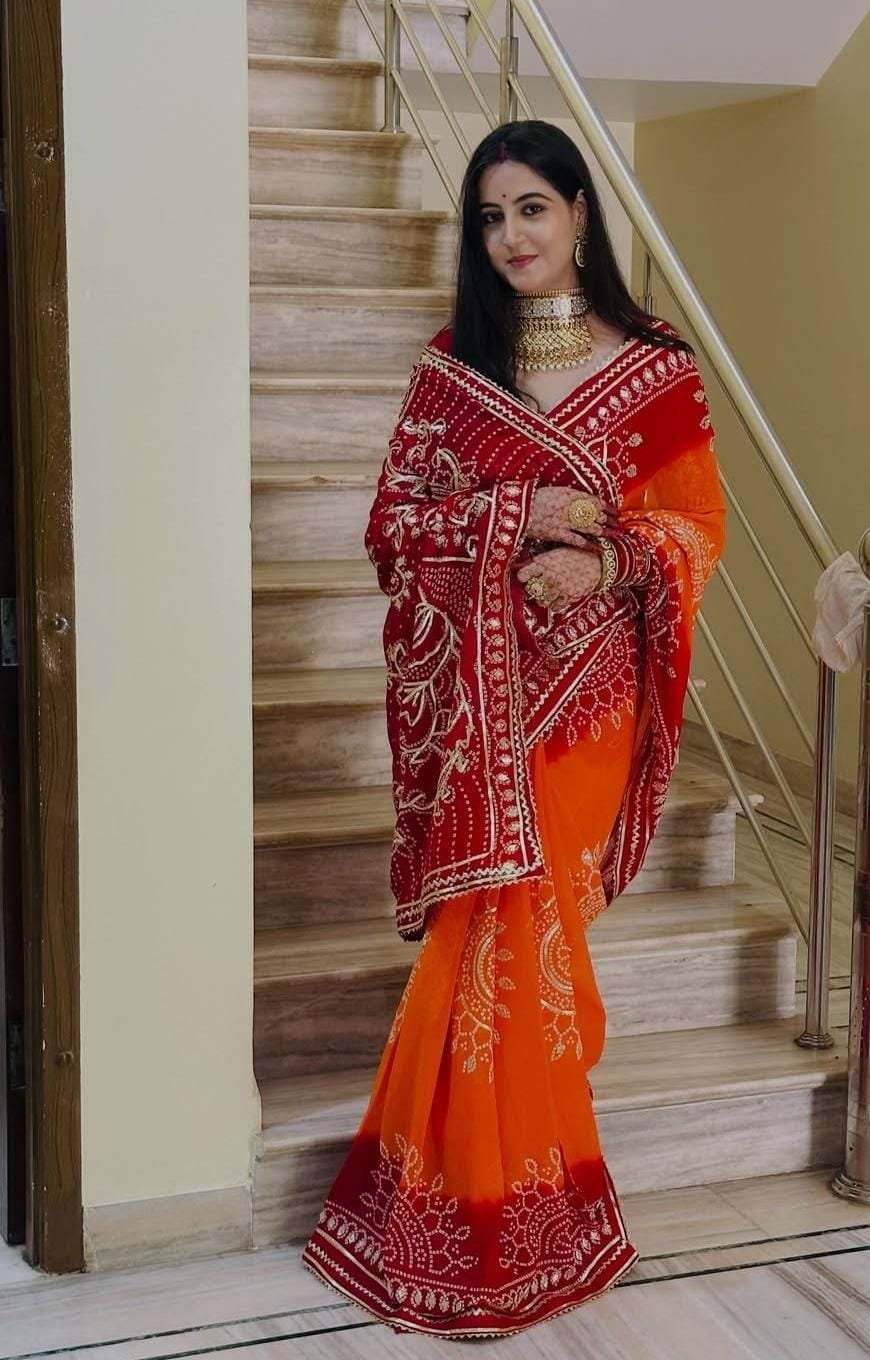 Piliya Saree in Georgette with Gota Patti Work 3 A woman wearing a vibrant orange and red Piliya saree with Gota Patti work standing on a staircase.