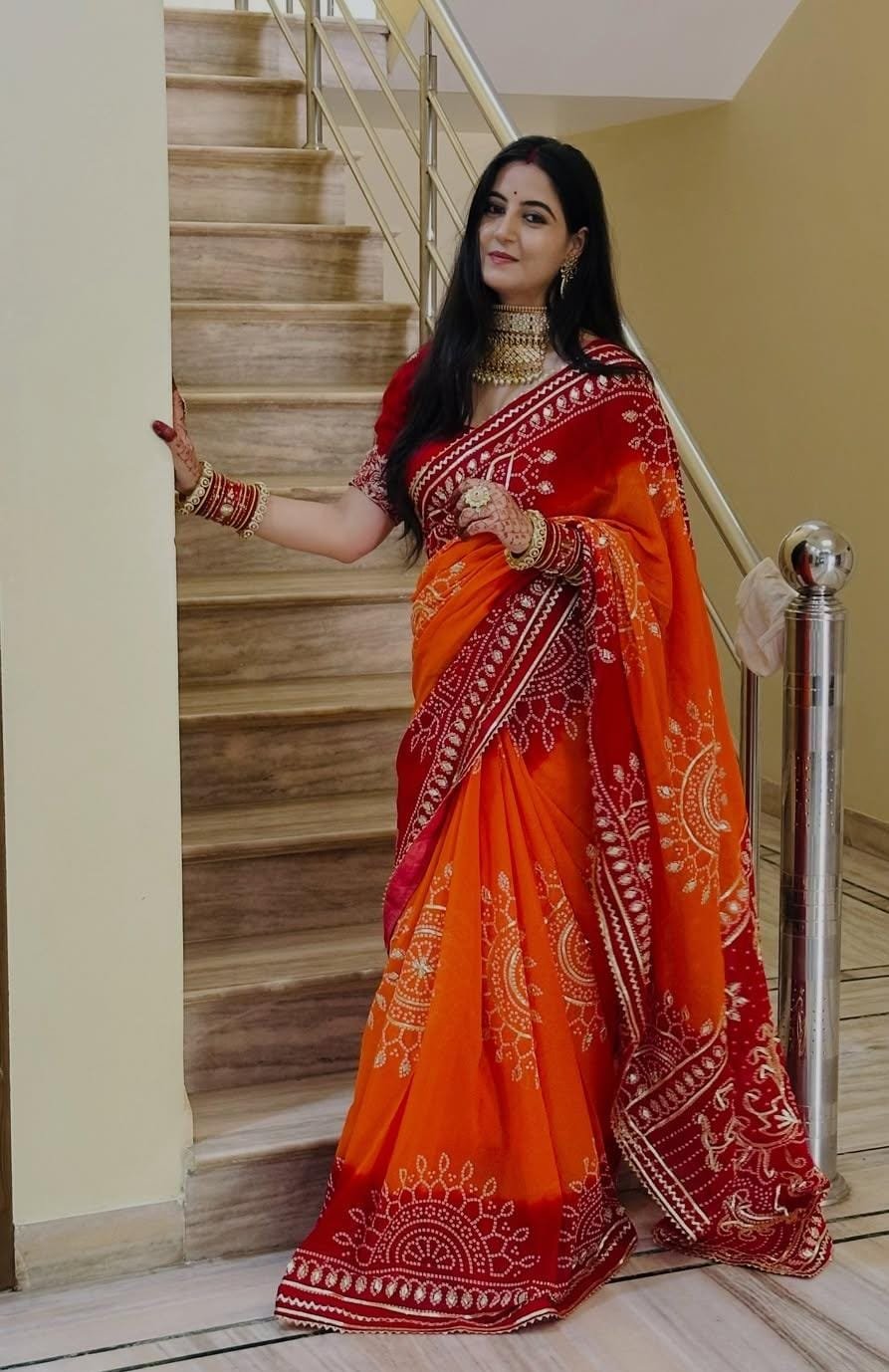 Piliya Saree in Georgette with Gota Patti Work 5 A woman wearing a vibrant orange and red Piliya saree with Gota Patti work standing on a staircase.