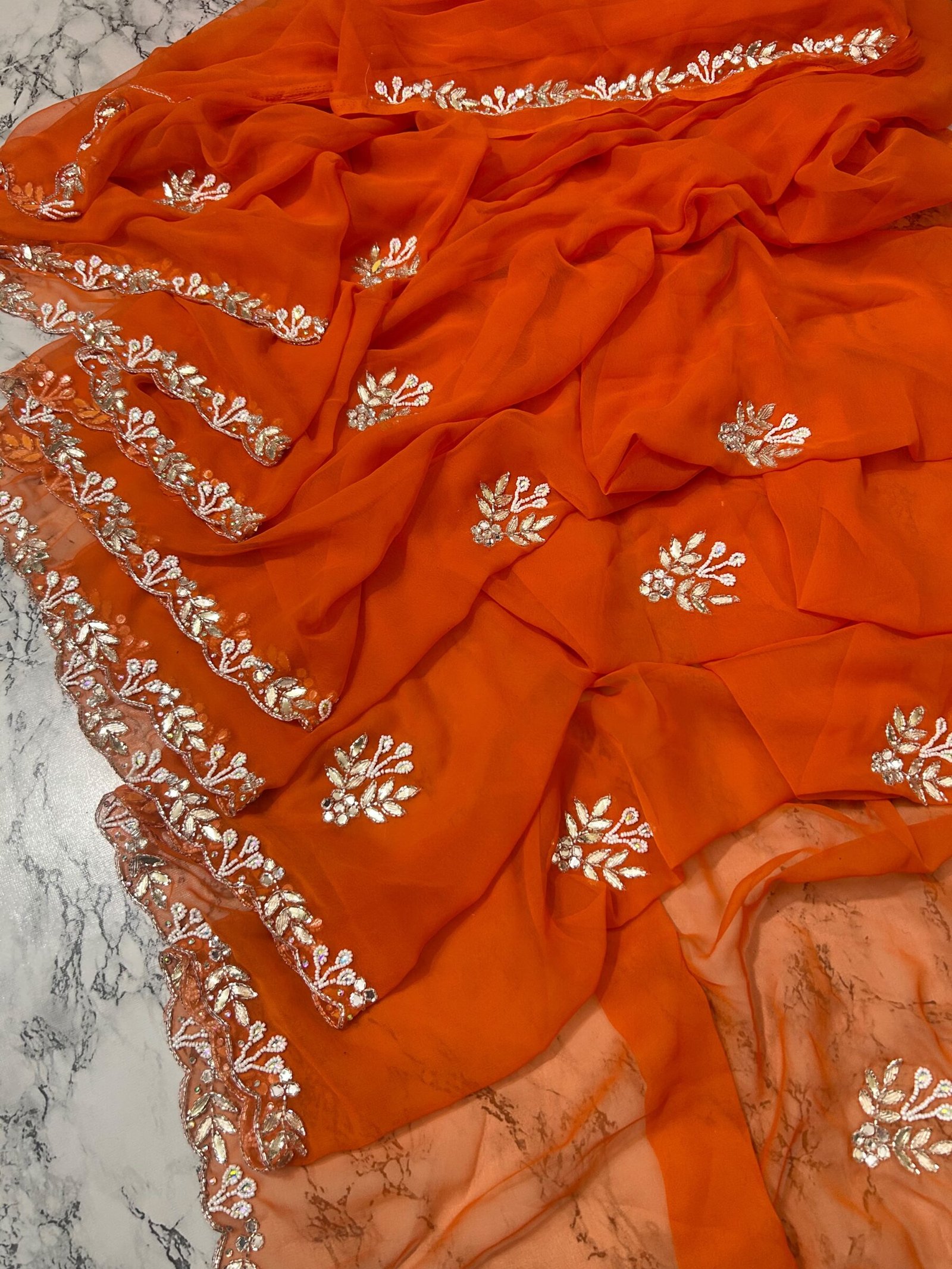 Orange Royal Georgette Handwork Saree with Cutwork Border 3 A vibrant orange Royal Georgette saree laid flat, featuring intricate white handwork floral motifs and a detailed cutwork border.