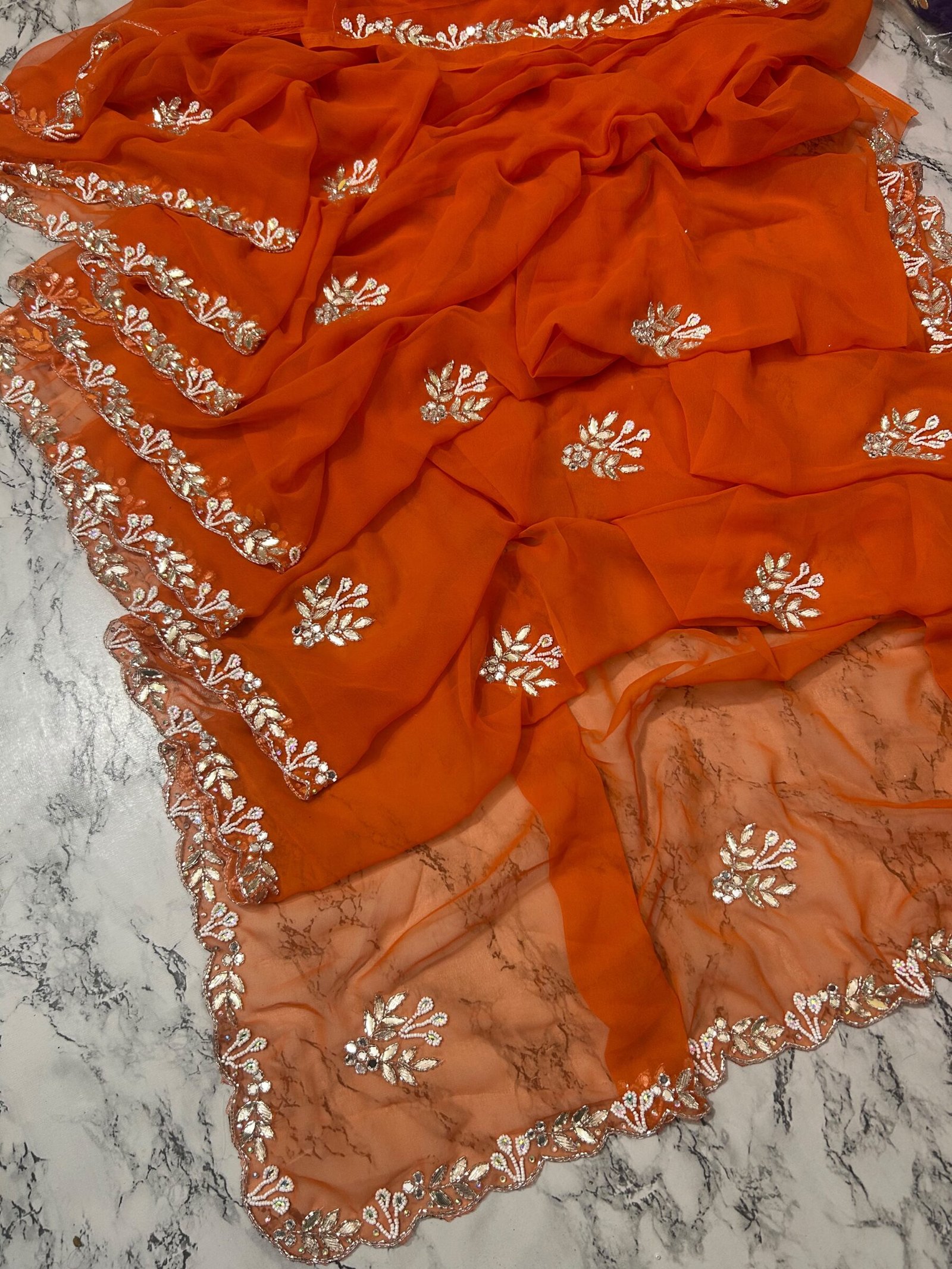 Orange Royal Georgette Handwork Saree with Cutwork Border 4 A vibrant orange Royal Georgette saree laid flat, featuring intricate white handwork floral motifs and a detailed cutwork border.