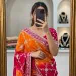 A woman wearing a vibrant orange and pink Russian crepe silk saree with elegant gota lace border and sequence embroidery.