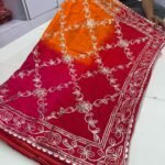 A woman wearing a vibrant orange and pink Russian crepe silk saree with elegant gota lace border and sequence embroidery.
