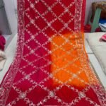 A woman wearing a vibrant orange and pink Russian crepe silk saree with elegant gota lace border and sequence embroidery.