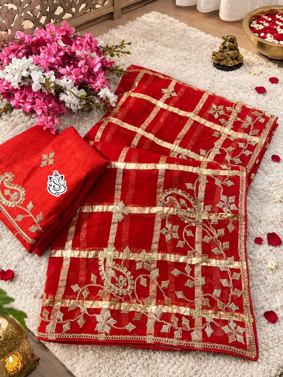 Red & Rani Soft Viscose Silk Pittawork Saree 1 A luxurious red soft viscose silk saree with gold grid patterns and intricate floral embroidery border displayed on a white fluffy rug.