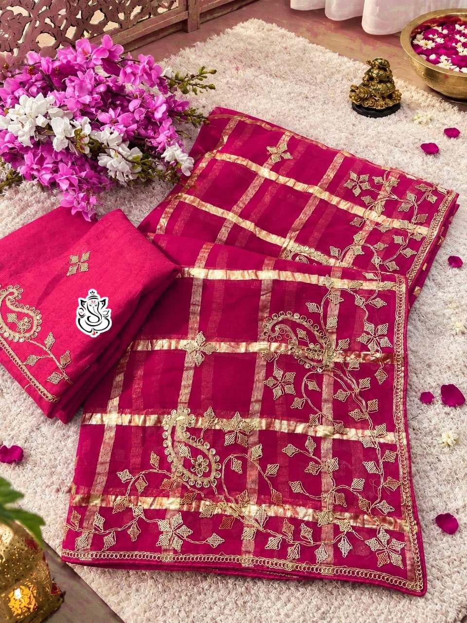 Red & Rani Soft Viscose Silk Pittawork Saree 2 A luxurious red soft viscose silk saree with gold grid patterns and intricate floral embroidery border displayed on a white fluffy rug.