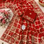 A luxurious red soft viscose silk saree with gold grid patterns and intricate floral embroidery border displayed on a white fluffy rug.