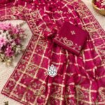 A luxurious red soft viscose silk saree with gold grid patterns and intricate floral embroidery border displayed on a white fluffy rug.