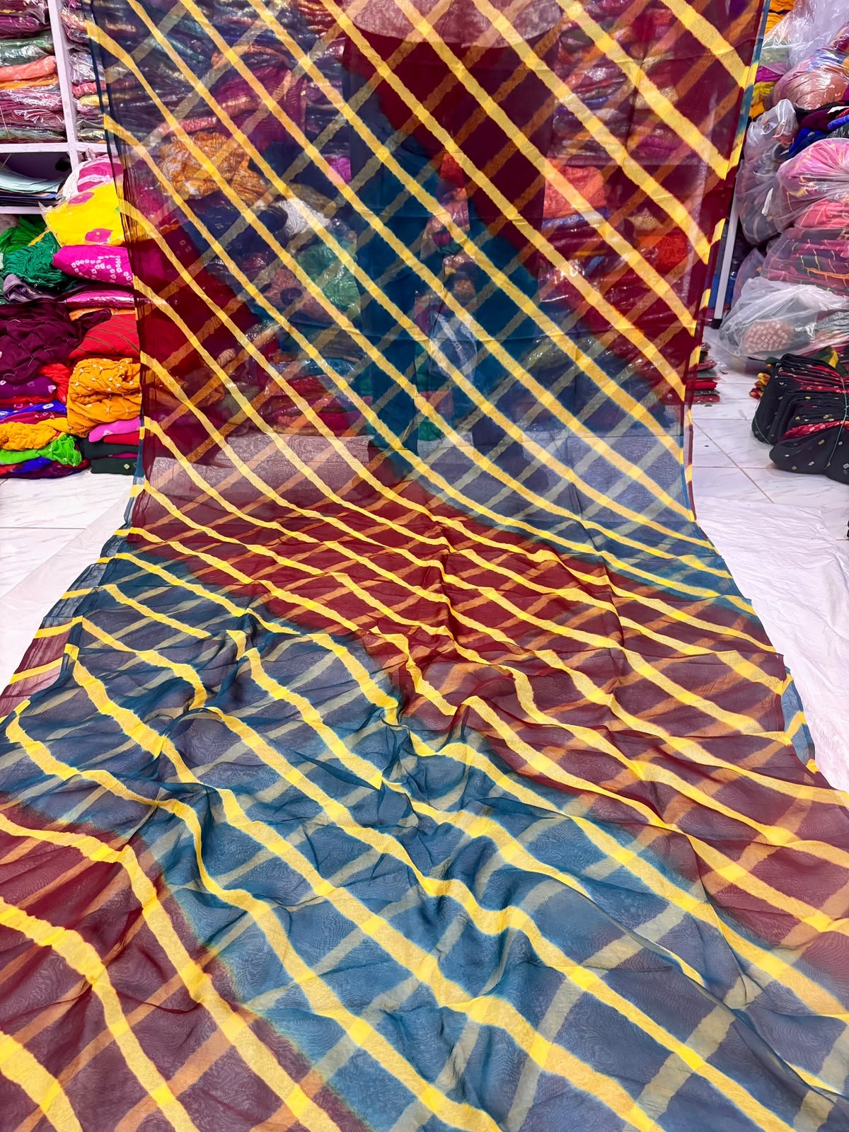 Tora Silk Leheriya Saree - Latest Casual Wear 2 A vibrant Tora Silk Leheriya saree featuring diagonal yellow, pink, and dark green stripes laid out on a white surface.