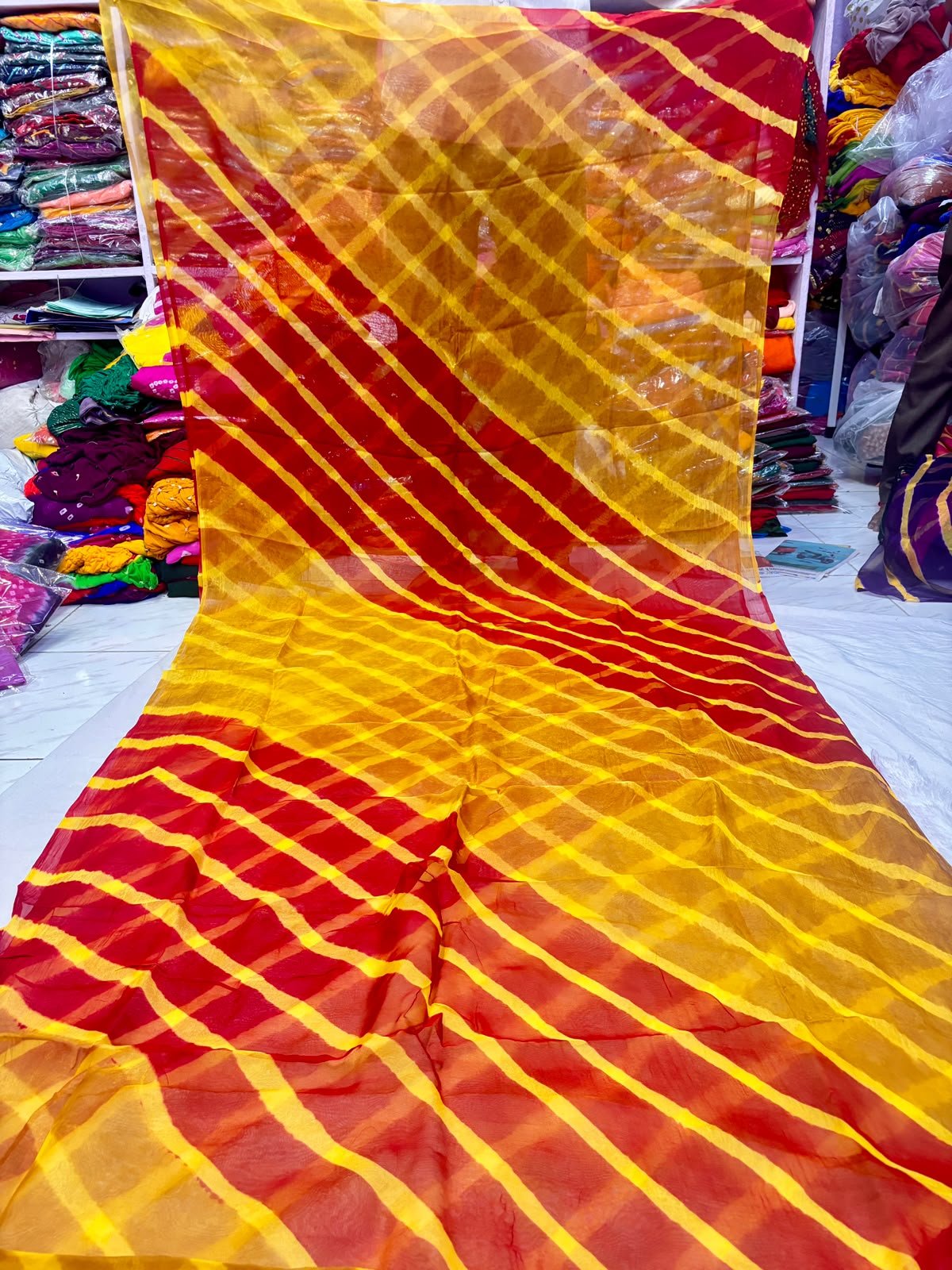 Tora Silk Leheriya Saree - Latest Casual Wear 4 A vibrant Tora Silk Leheriya saree featuring diagonal yellow, pink, and dark green stripes laid out on a white surface.