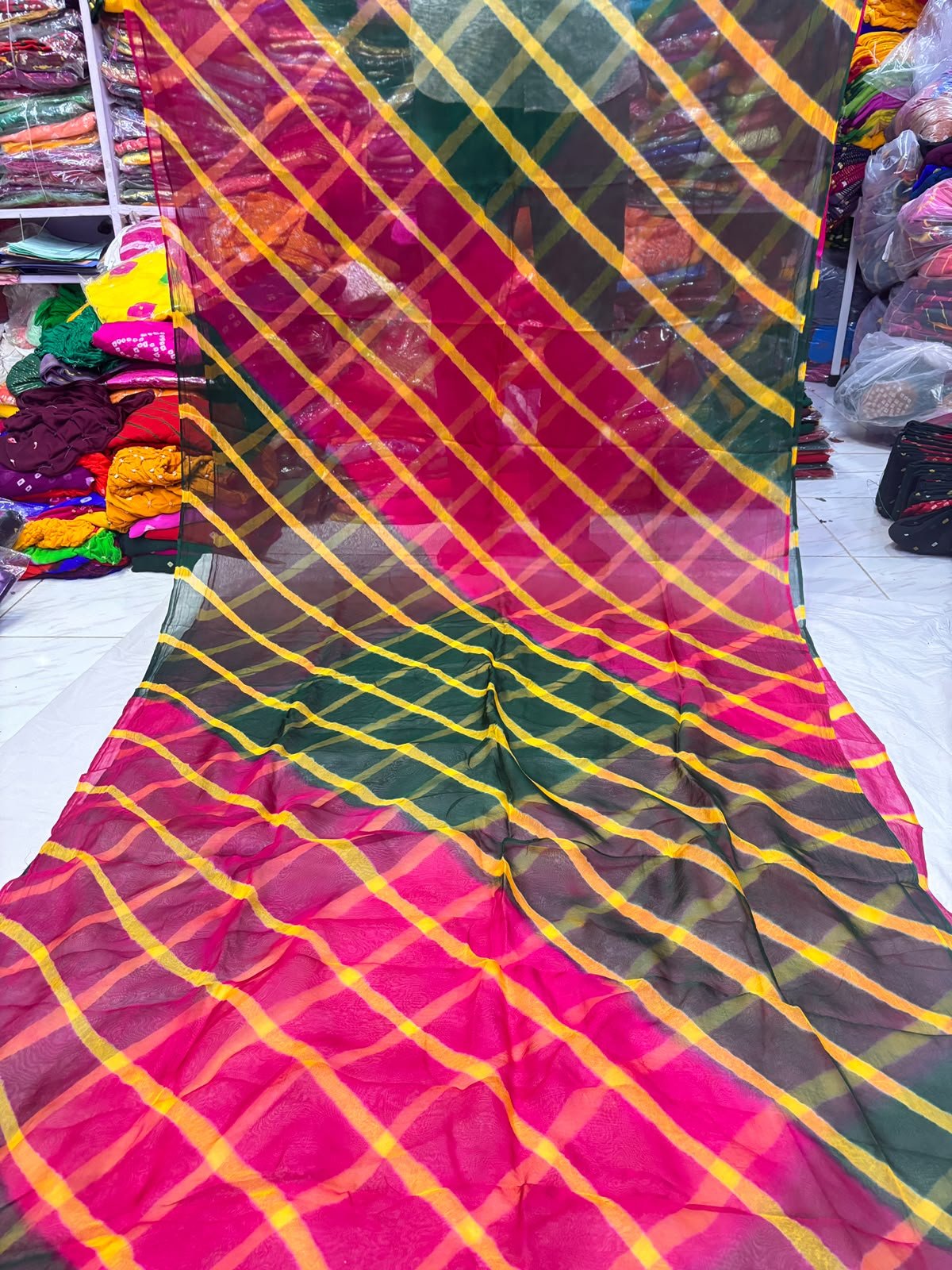 Tora Silk Leheriya Saree - Latest Casual Wear 5 A vibrant Tora Silk Leheriya saree featuring diagonal yellow, pink, and dark green stripes laid out on a white surface.