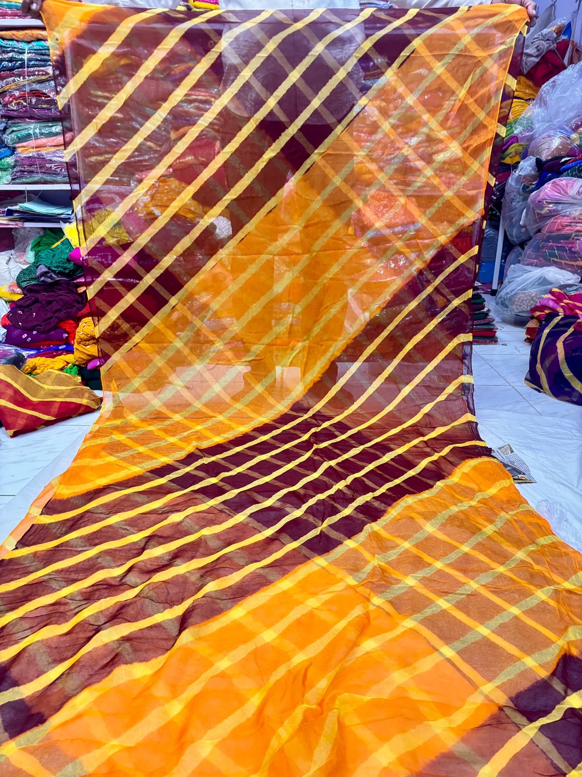 Tora Silk Leheriya Saree - Latest Casual Wear 6 A vibrant Tora Silk Leheriya saree featuring diagonal yellow, pink, and dark green stripes laid out on a white surface.
