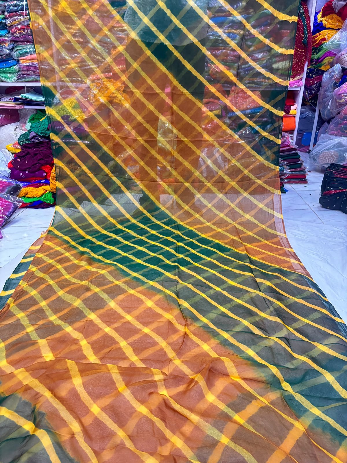 Tora Silk Leheriya Saree - Latest Casual Wear 7 A vibrant Tora Silk Leheriya saree featuring diagonal yellow, pink, and dark green stripes laid out on a white surface.