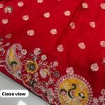 A person holds up a red Upada silk saree featuring a detailed border with multi-sequence work and round peacock motifs.