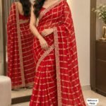 A beautiful woman posing in a red Viscose Chokda saree featuring a grid pattern and detailed embroidery border.