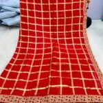 A beautiful woman posing in a red Viscose Chokda saree featuring a grid pattern and detailed embroidery border.