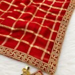 A beautiful woman posing in a red Viscose Chokda saree featuring a grid pattern and detailed embroidery border.